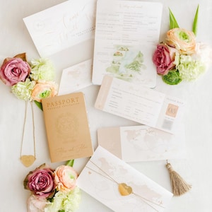 Puede incluir: Un conjunto de invitaciones de boda con temática de viaje. La invitación presenta un diseño de pasaporte con un mapa del mundo y el texto "Come Fly With Us" en caligrafía. La tarjeta RSVP presenta un diseño de tarjeta de embarque con el texto "Please RSVP" y un número de vuelo. La invitación está decorada con flores rosas y blancas.