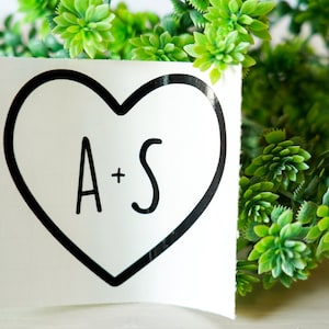 May include: A white sticker with a black outline of a heart. Inside the heart is the text "A+S" in black.