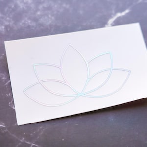 May include: A white sticker with a holographic lotus flower design. The flower is outlined in a silver color.