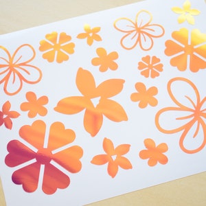 May include: A sheet of orange and gold holographic sticker paper with various flower shapes cut out. The flowers are in different sizes and have a shiny, iridescent finish.