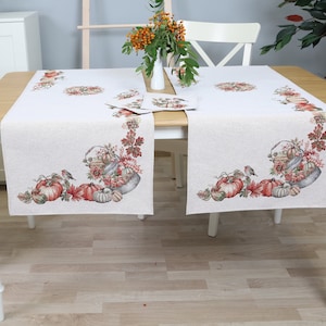 Peut inclure: Une table blanche avec deux chaises blanches et un chemin de table beige avec un motif d'automne représentant des citrouilles, des feuilles et des oiseaux. Le chemin de table a une bordure brune.