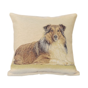 Puede incluir: Una almohada beige con una imagen tejida de un perro Collie acostado, en tonos marrones y blancos.