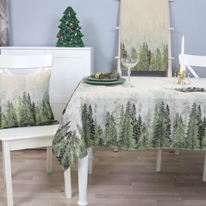 May include: A white table with a green and white tablecloth featuring a forest scene. The tablecloth has a repeating pattern of pine trees. There is a white chair with a cushion featuring the same forest scene as the tablecloth.
