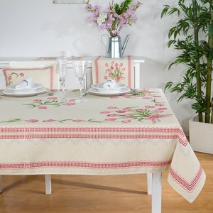 Könnte beinhalten: Eine weiße Tischdecke mit einem pinkfarbenen Tulpenmuster und einem roten und weißen Rand. Die Tischdecke liegt auf einem weißen Tisch mit vier Gedecken. An jedem Gedeck stehen zwei Gläser und ein Teller.