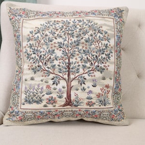 May include: Square decorative pillow with a detailed tapestry design. The pillow features a central tree motif with blue-green leaves and a brown trunk, surrounded by floral and foliage elements in a muted color palette. The border has a floral pattern.