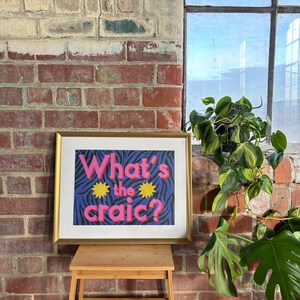 May include: A framed print with a purple and black zebra print background. The text "What's the craic?" is in pink and yellow letters.