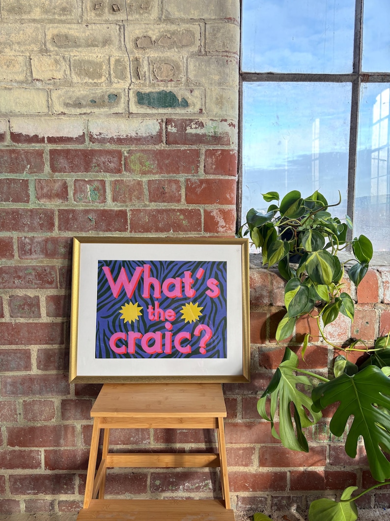 May include: A framed print with a purple and black zebra print background. The text "What's the craic?" is in pink and yellow letters.