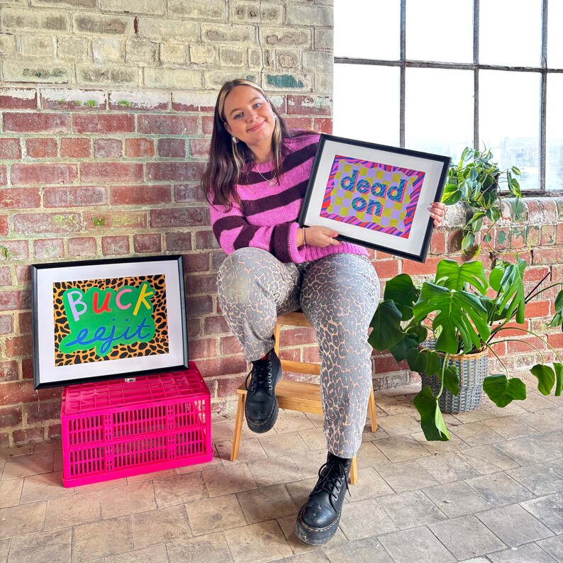 May include: Two framed prints with colorful text and patterns. The print on the left says "buck eejit" and the print on the right says "dead on".
