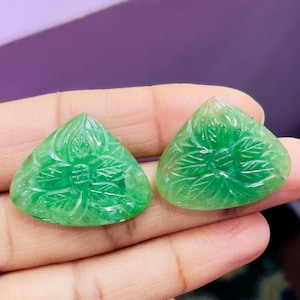 May include: Two green gemstone carvings shaped like triangles with a flower design. The carvings are smooth and polished.