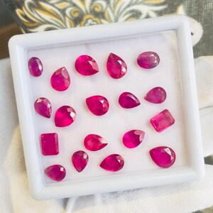 May include: A white tray with 18 pink ruby gemstones of various shapes and sizes.