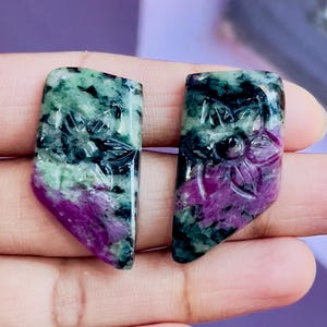 Op de afbeelding: Twee gegraveerde groene en roze edelsteen cabochons met een bloemmotief. De cabochons zijn gezet in een ruwe, natuurlijke stijl.