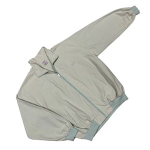 May include: A light beige zip-up jacket with a light blue zipper and trim. The jacket has a stand-up collar and a ribbed hem.