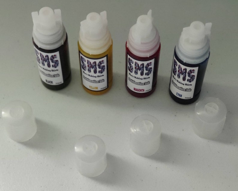 May include: Four small bottles of sublimation ink, labeled with the colors black, yellow, magenta, and cyan. The bottles are arranged in a row, with their caps removed and placed below them.