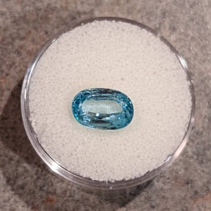 K&ouml;nnte beinhalten: Ein hellblauer ovaler Edelstein in einem durchsichtigen Plastikbeh&auml;lter auf einer wei&szlig;en Oberfl&auml;che.