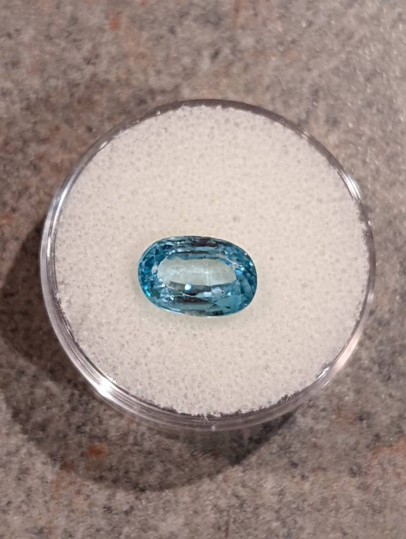 K&ouml;nnte beinhalten: Ein hellblauer ovaler Edelstein in einem durchsichtigen Plastikbeh&auml;lter auf einer wei&szlig;en Oberfl&auml;che.