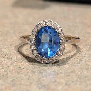 May include: A silver ring with a large oval blue gemstone surrounded by a halo of smaller diamonds.