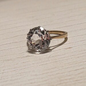 May include: A gold ring with a large, clear, faceted gemstone.