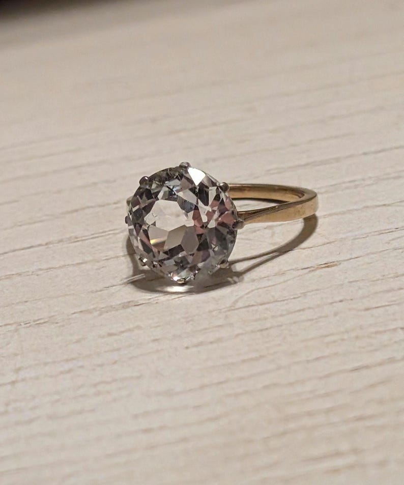 May include: A gold ring with a large, clear, faceted gemstone.