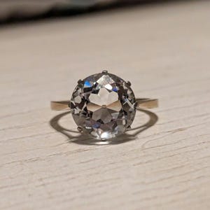 May include: A gold ring with a large, clear, faceted gemstone.