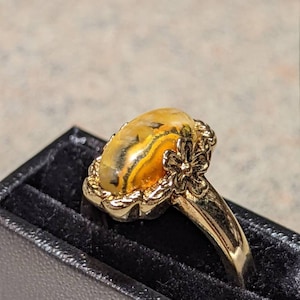 May include: A gold ring with a yellow agate stone set in a floral design. The ring is in a black velvet ring box.