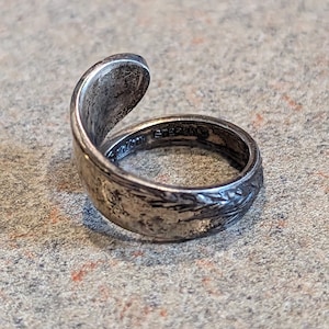 Puede incluir: Un anillo de plata hecho de una cuchara doblada. El anillo está grabado con un diseño floral y las palabras "Sterling" y "925".