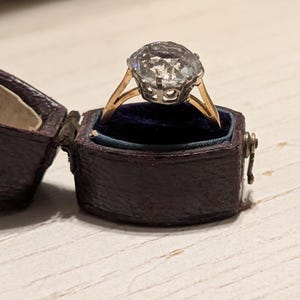 May include: A vintage ring with a large, clear, faceted gemstone set in a gold setting. The ring is in a dark blue velvet ring box.
