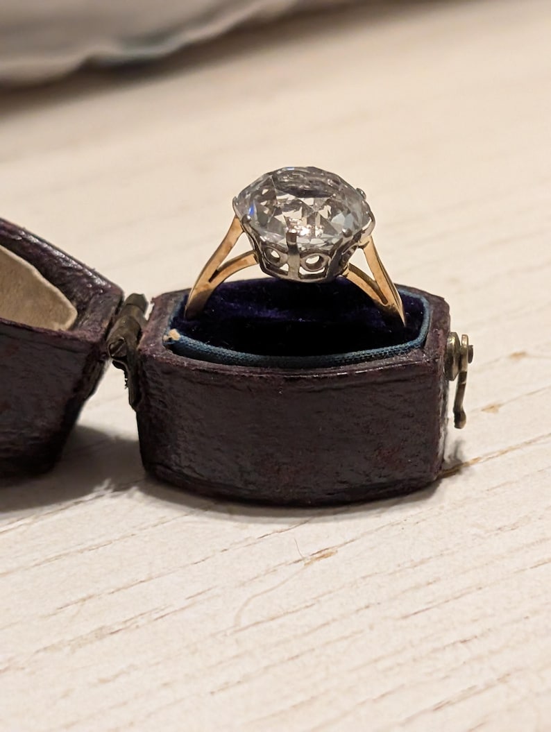 May include: A vintage ring with a large, clear, faceted gemstone set in a gold setting. The ring is in a dark blue velvet ring box.