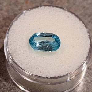 K&ouml;nnte beinhalten: Ein hellblauer ovaler Edelstein in einem durchsichtigen Plastikbeh&auml;lter mit einer wei&szlig;en Schaumstoffpolsterung.
