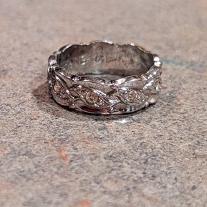 May include: A silver band ring with a decorative design featuring small clear stones.
