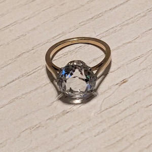 May include: A gold ring with a large, clear, oval-shaped gemstone.