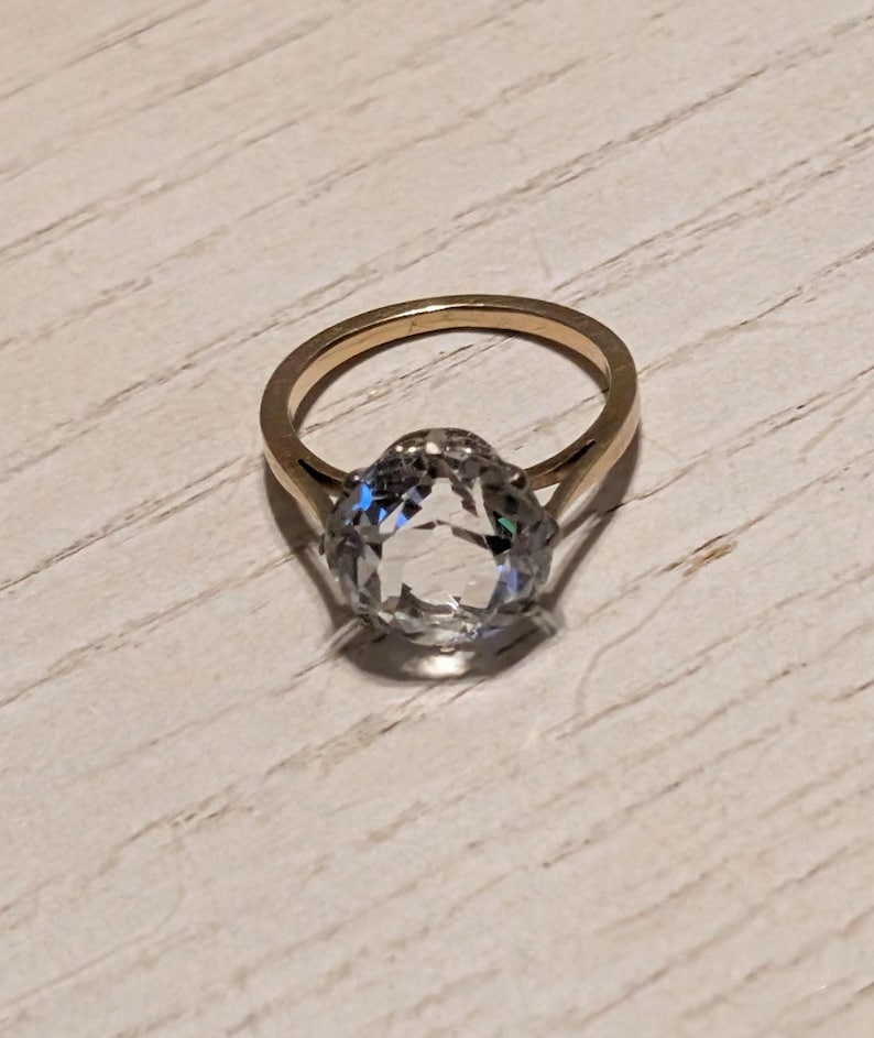 May include: A gold ring with a large, clear, oval-shaped gemstone.