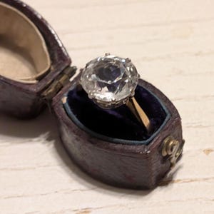 May include: A vintage ring with a large, clear, faceted gemstone set in a gold band. The ring is in a velvet-lined box.