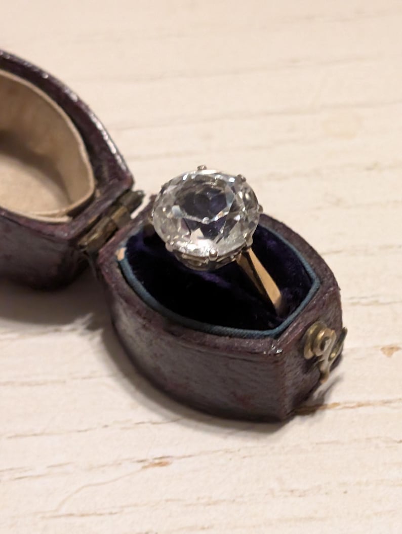 May include: A vintage ring with a large, clear, faceted gemstone set in a gold band. The ring is in a velvet-lined box.