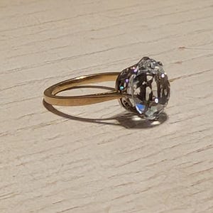 May include: A gold ring with a large, clear, oval-shaped gemstone.