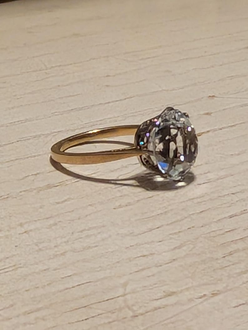 May include: A gold ring with a large, clear, oval-shaped gemstone.