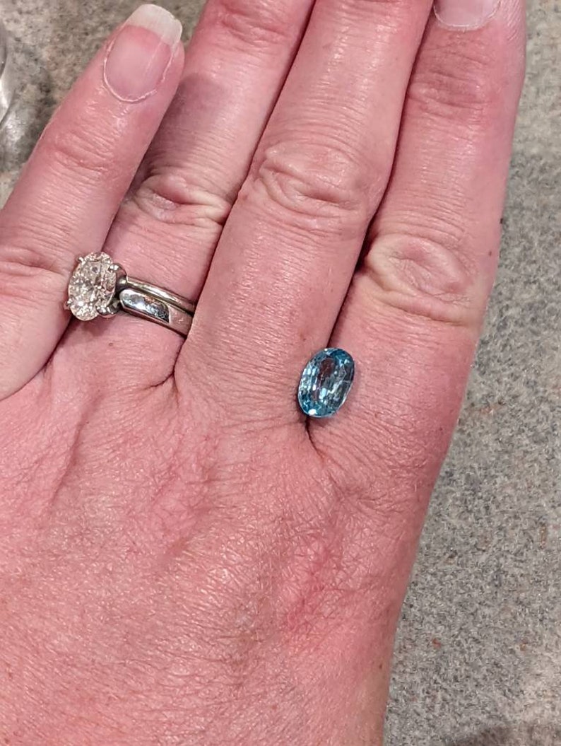 K&ouml;nnte beinhalten: Ein ovaler, hellblauer Edelstein mit Facetten auf einer Hand.