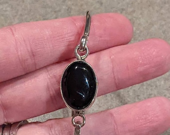 May include: A silver bangle bracelet with a black oval gemstone. The bracelet is open and has a simple design.