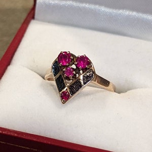 May include: A gold ring with a heart-shaped design set with five red rubies. The ring is in a red velvet box.