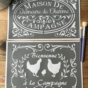 Puede incluir: Dos plantillas grises con diseños y texto blancos. Una plantilla dice "MAISON DE Demeure de Charme CAMPAGNE" en un marco ovalado. La otra dice "Bienvenue à la Campagne" con siluetas de gallinas. Hay pinceles a un lado.