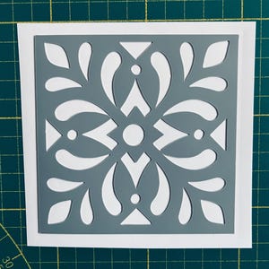 May include: A grey stencil with a white cutout design of a geometric pattern. The stencil is on a white background.
