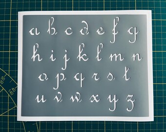 May include: A white stencil with a gray background featuring the alphabet in a cursive font.