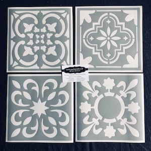 Może przedstawiać: Cztery szablony do płytek w kolorze szarym z białymi wzorami. Szablony przedstawiają różne geometryczne wzory, w tym gwiazdę, koło i krzyż.