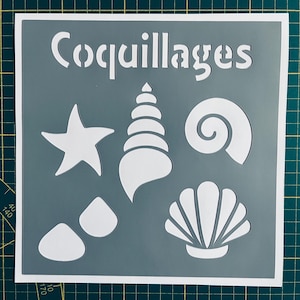 May include: A white stencil with the word "Coquillages" and images of seashells, a starfish, and pebbles. The stencil is on a gray background.