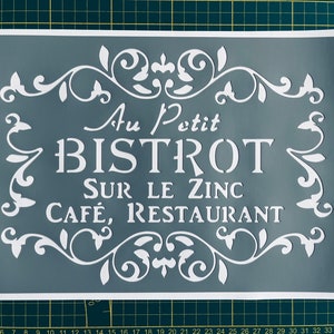 Peut inclure: Un pochoir blanc sur fond gris avec le texte "Au Petit Bistrot Sur Le Zinc Cafe, Restaurant" dans une police décorative.