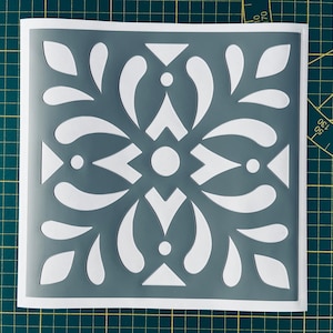 Może przedstawiać: Szablon szary z białym wzorem stylizowanego wzoru kwiatowego. Szablon jest kwadratowy i ma ozdobną ramkę.