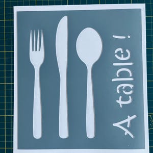 Peut inclure: Un pochoir blanc sur un fond gris avec une fourchette, un couteau et une cuillère, et le texte "A table!"
