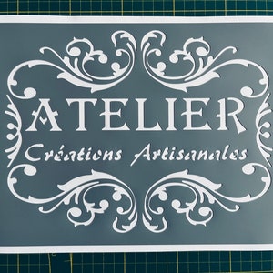 Puede incluir: Una plantilla blanca sobre un fondo gris con el texto "ATELIER Creaciones Artesanales" en una fuente decorativa.