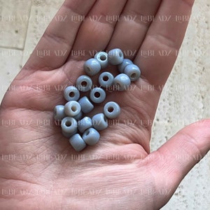 May include: A pile of light blue plastic beads, scattered on a hand.