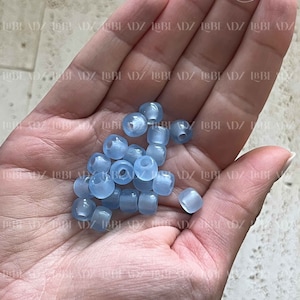 May include: A hand holding a pile of light blue plastic beads. The beads are round and have a smooth, glossy finish.