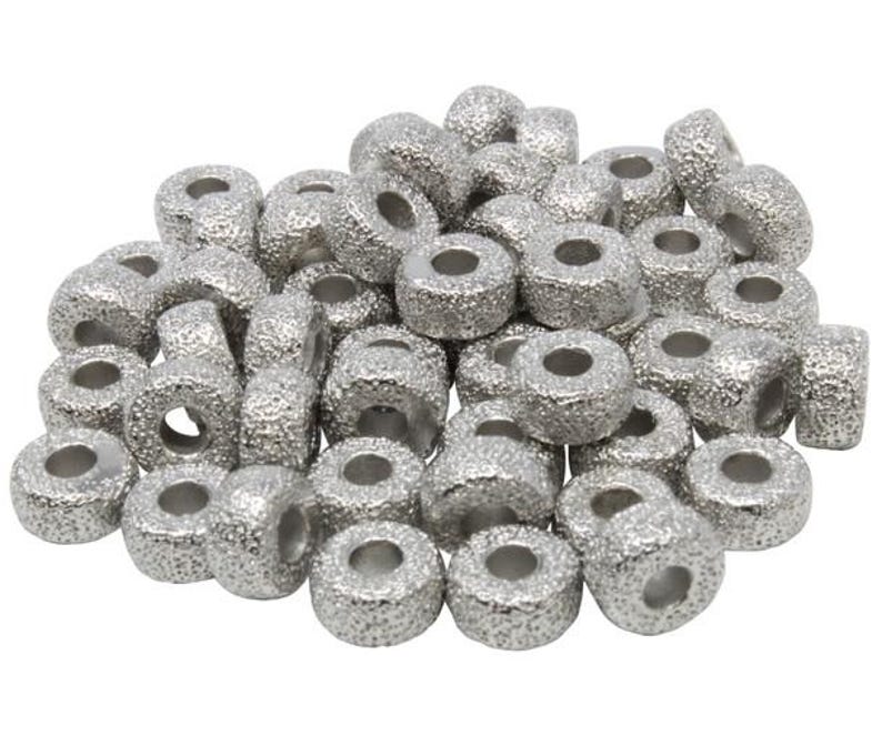 Op de afbeelding: Een stapel zilverkleurige metalen kralen met een getextureerd oppervlak. De kralen zijn rond met een gat in het midden.